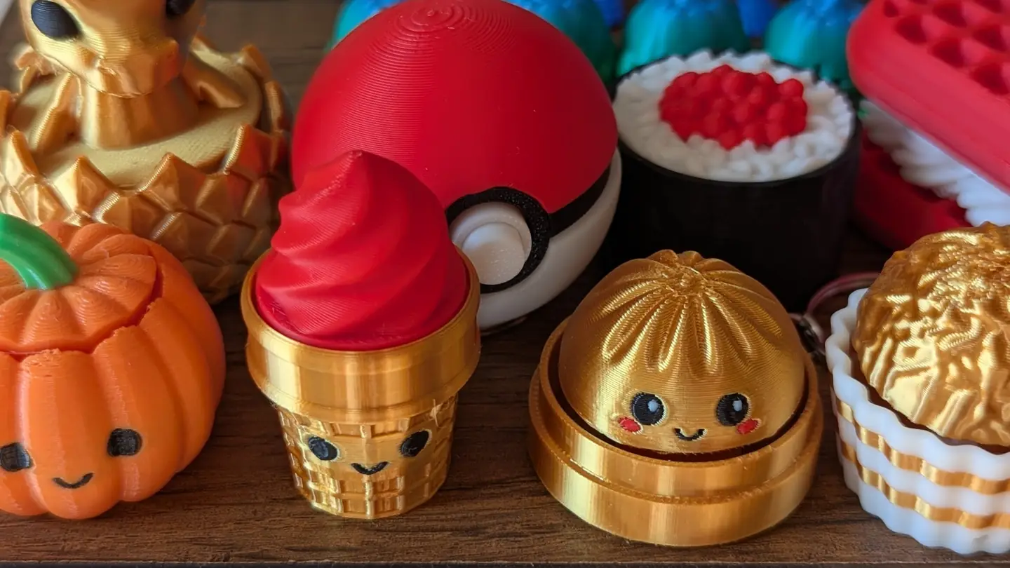 A collection of colorful 3D by 3 prints, including a gold dragon, pumpkin, ice-cream cone and dumpling.
